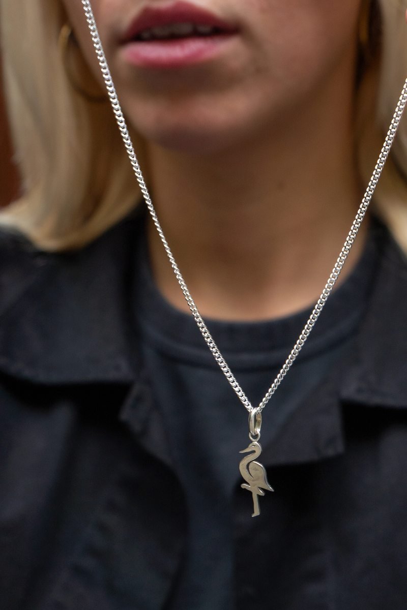 Zilveren ooievaarhanger aan een zilveren ketting op een zwarte blouse